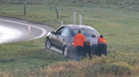 Omstanders helpen een automobilist die van de weg is geraakt.