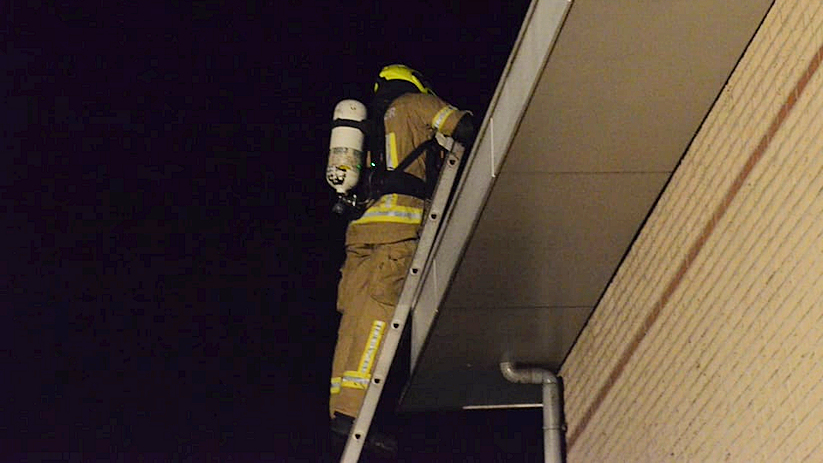 Een brandweerman inspecteert de dakgoot.