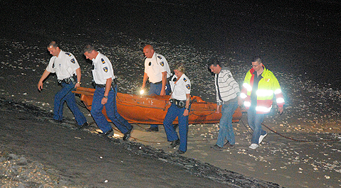 Strandwachten en politiemensen tillen het bootje de dijk op.